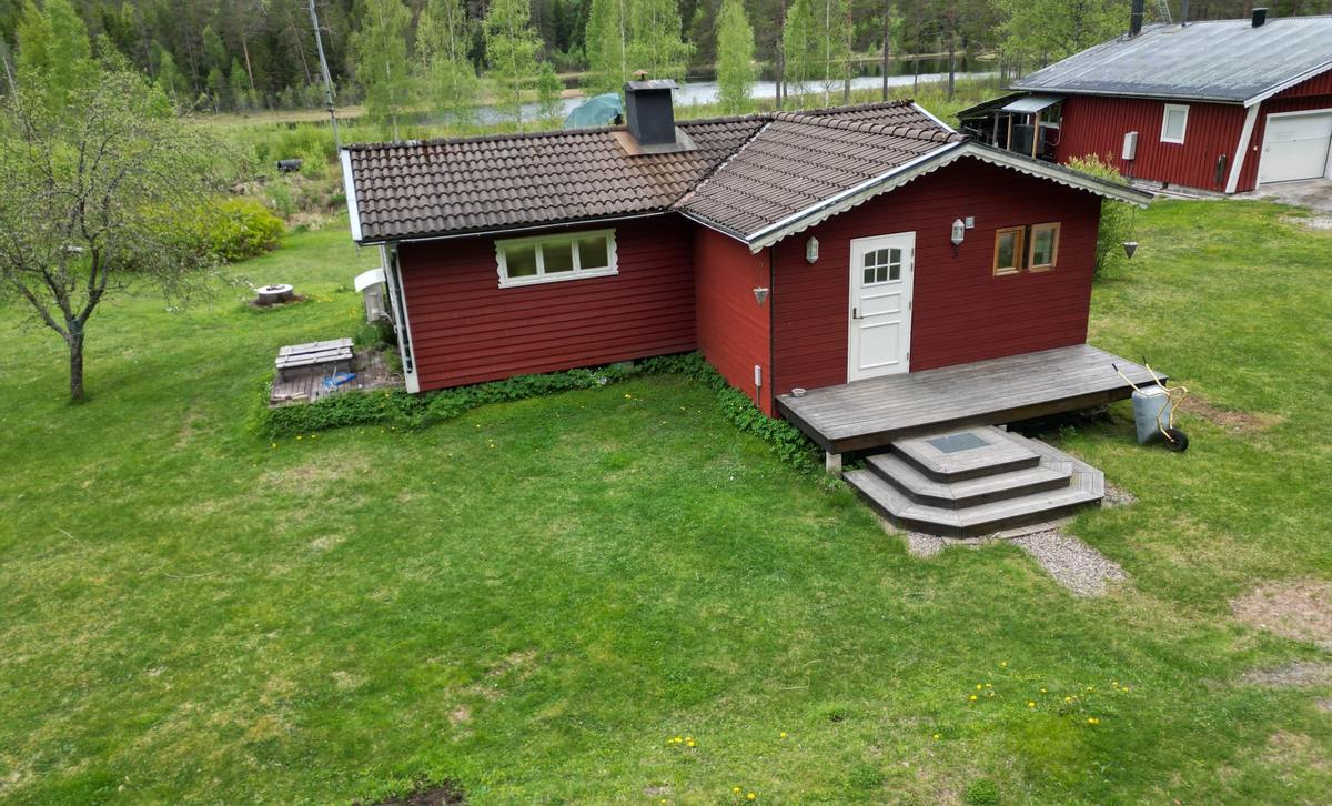 Rött hus med vit dörr, gräsmatta och skog